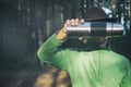 Faceless portrait of bearded tourist man in felt hat holding stainless thermos in front of his face on woods background. Hiker on