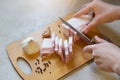 Faceless portrait of woman cutting lard with layers of meat on wooden cutting board among some garlic, peppercorns on white table