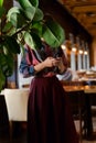 Faceless portrait of a young woman with smartphone in restaurant hall , face hidden by leaves of a green plant