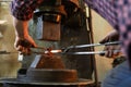 Crop blacksmith pressing hot metal stick in grungy smithy