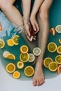 Faceless shot of woman in a bathroom filled with blue water and various cut citrus fruits holding serum in her hands Royalty Free Stock Photo