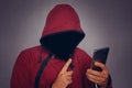 Silhouette of a man in a hood on a black background, his face is not visible, the hacker is holding the phone in his hands. The co Royalty Free Stock Photo