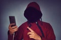 Faceless unrecognizable hooded person using mobile phone, identity theft and technology crime concept, selective focus