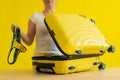Faceless woman folds bikini in a suitcase on a yellow background. The girl is packing luggage for a trip to the trip to