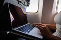 Faceless woman in a mask works on a laptop on an airplane while sitting by the window during the flight. Freelancer on a