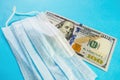 Facemask on banknote of 100 dollars on blue background. Medical mask price increase concept, protect against coronavirus