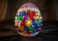 A faceted, egg-shaped object covered in colorful gemstones and crystals is displayed on a dark Royalty Free Stock Photo