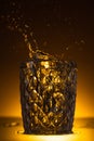 Faceted glass with splashing vodka in dark with warm back light. Royalty Free Stock Photo