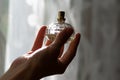 Faceted glassy charm bottle of feminine toilette water in young woman hand. Floral fragrance lit by light.