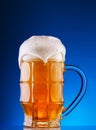 Faceted mug of the light beer with foam on blue background Royalty Free Stock Photo