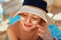 Facial Care. Female Applying Sun Cream and Smiling. Beauty Face. Portrait Of Young Woman in hat Smear Moisturizing Lotion on Skin. Royalty Free Stock Photo