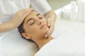 Positive relaxed woman getting procedure of facial massage from cosmetologists hands