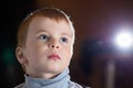 Facial portrait of dreamy pensive blond boy with gaze his eyes fixed upwards over dark background with specks of dust flying in Royalty Free Stock Photo