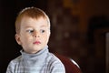 Facial portrait of scared pensive blond boy looking away with fear over dark background with specks of dust flying in