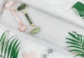 Facial roller from crystal rose quartz and massage tool jade Gua sha on the tray on grey background with palm leaves.