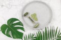Facial roller from crystal rose quartz and massage tool jade Gua sha on the tray on grey background with palm leaves.