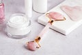 Facial roller, gua sha, serum and moisturizing cream on marble background