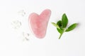 Facial scraper of natural guasha stone and green leaves on white background