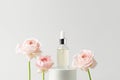 Facial serum in glass dropper bottle on white podium and pink roses on grey background. Natural skin care cosmetic Royalty Free Stock Photo