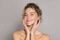 Facial skincare. Happy beautiful lady touching face, moisturizing smooth skin and smiling at camera, grey background Royalty Free Stock Photo