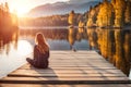 Facing back young woman , sitting on wooden pier on shore beautiful mountain lake at sunrise or Royalty Free Stock Photo