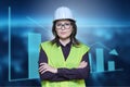 Factory engineer woman in safety helmet vest posing on industrial background with graphs