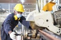 A factory mechanic is using a chainsaw to cut copper pipes. An expert technician is inspecting industrial machinery in a steel