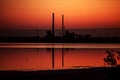 Factory pipes are reflected in the water, sunset painted the sky and water in orange Royalty Free Stock Photo