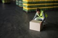 Man in safety vest crouching and lifting box by pallets of bottles in warehouse, copy space Royalty Free Stock Photo
