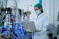 Factory worker woman with gown and hygiene mask hold laptop to control the machine in factory workplace