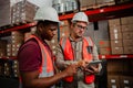 Factory workers browsing through delivery tracking on digital tablet standing besides parcels in warehouse. Royalty Free Stock Photo