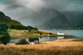 A faded rainbow hovers above a calm farming and fishing village in remote Norway. hazy mountain background makes for a dramatic