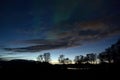 Faint aurora borealis dancing over fjord and trees