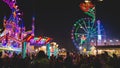 Fair crowded with attractions, colorful lights and ferris wheel at night. Part of ferris wheel against a dark sky background with