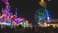 Fair crowded with attractions, colorful lights and ferris wheel at night. Part of ferris wheel against a dark sky background with