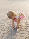 Fair-haired baby in tennis clothes ties shoelaces at sunset