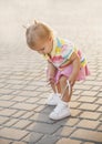 Fair-haired baby in tennis clothes ties shoelaces at sunset