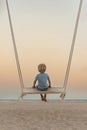 Fair-haired boy sits on swing above sea shore on sunset. Magic surreal zen landscape. Romantic pink twilight Royalty Free Stock Photo