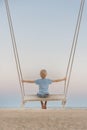 Fair-haired boy sits on swing above sea shore on sunset. Magic zen landscape. Romantic pink twilight Royalty Free Stock Photo