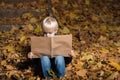 Fair haired boy sitting on autumn leaves in forest and holds large book in hands. Children`s education