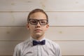 A fair-haired boy of 10 years in a white shirt with the self-tie bow tie with a serious expression on the background of a wooden Royalty Free Stock Photo