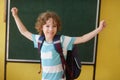 The fair-haired curly school student stand against a blackboard.