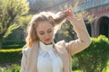 Fair-haired girl in beige coat walking in the park on sunny spring day. Portrait of modern young woman outdoors Royalty Free Stock Photo