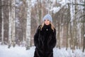 fair-haired girl in a blue hat, black fur coat against the backdrop of a snowy winter birch forest Royalty Free Stock Photo