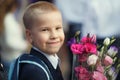 a fair-haired little boy, a schoolboy, with a bouquet of bright flowers smiles and looks at the camera