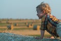 A fair-haired littleboy sits on top of a straw bale on a wheat field