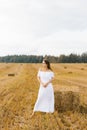A fair haired young woman farmer in a white dress in a field with stacks of straw enjoys a summer day Royalty Free Stock Photo