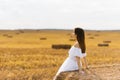 A fair haired young woman farmer in a white dress in a field with stacks of straw enjoys a summer day Royalty Free Stock Photo