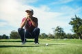 On the fairway. a focused young male golfer looking at a golf ball while being seated on the grass outside during the Royalty Free Stock Photo