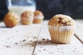 Fairy cakes baked with some sessame seeds on a white wooden table against a black background in a rustic kitchen. Jar of milk